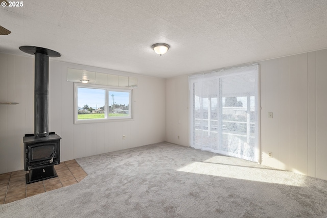 unfurnished living room featuring a textured ceiling, carpet, and a wood stove