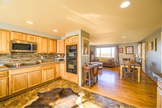 kitchen with light brown cabinetry, tasteful backsplash, light hardwood / wood-style flooring, and black appliances