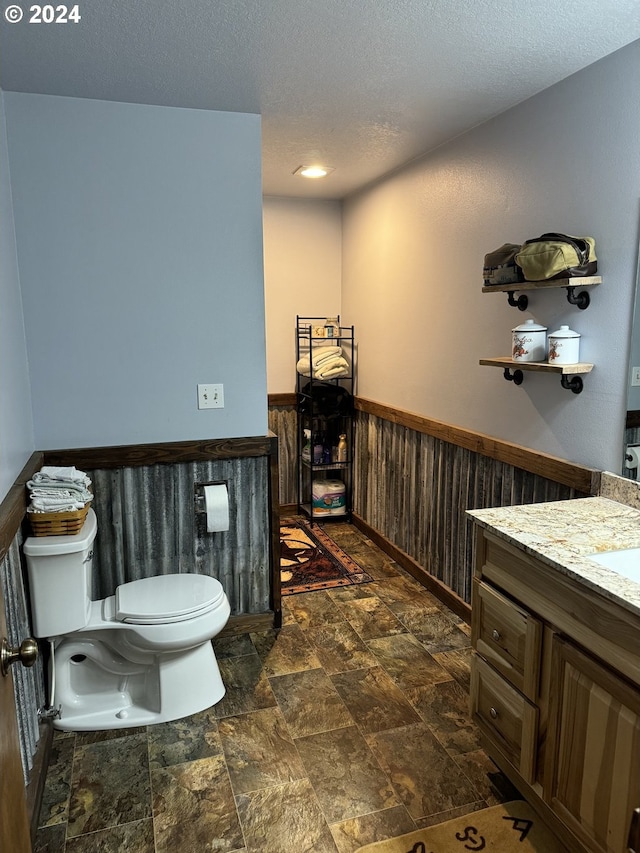 bathroom with wooden walls, vanity, a textured ceiling, and toilet