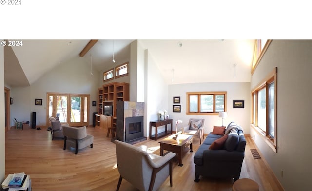 living room with a fireplace, high vaulted ceiling, a healthy amount of sunlight, and light wood-type flooring