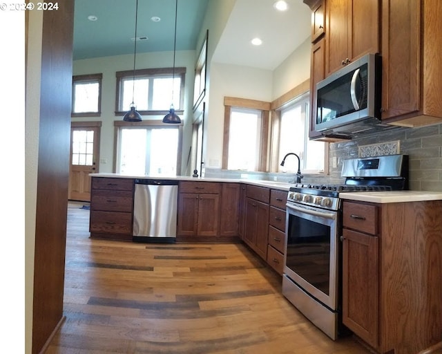 kitchen featuring sink, hanging light fixtures, stainless steel appliances, tasteful backsplash, and hardwood / wood-style floors