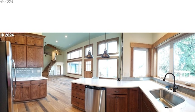 kitchen featuring hanging light fixtures, sink, light wood-type flooring, appliances with stainless steel finishes, and tasteful backsplash