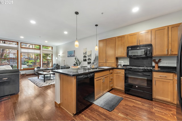 kitchen with dark stone countertops, black appliances, hanging light fixtures, kitchen peninsula, and dark wood-type flooring