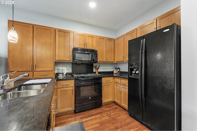 kitchen with black appliances, hanging light fixtures, dark stone counters, dark hardwood / wood-style floors, and sink