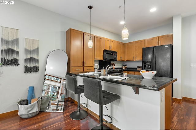 kitchen featuring sink, a kitchen bar, hanging light fixtures, black appliances, and dark wood-type flooring