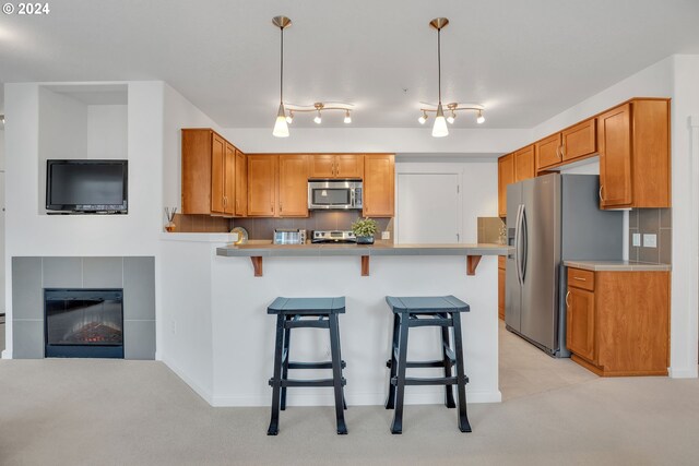 kitchen featuring kitchen peninsula, stainless steel appliances, backsplash, decorative light fixtures, and a fireplace