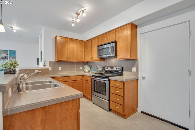 kitchen with sink, kitchen peninsula, hanging light fixtures, stainless steel appliances, and decorative backsplash