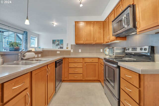 kitchen featuring stainless steel appliances, decorative backsplash, sink, and hanging light fixtures