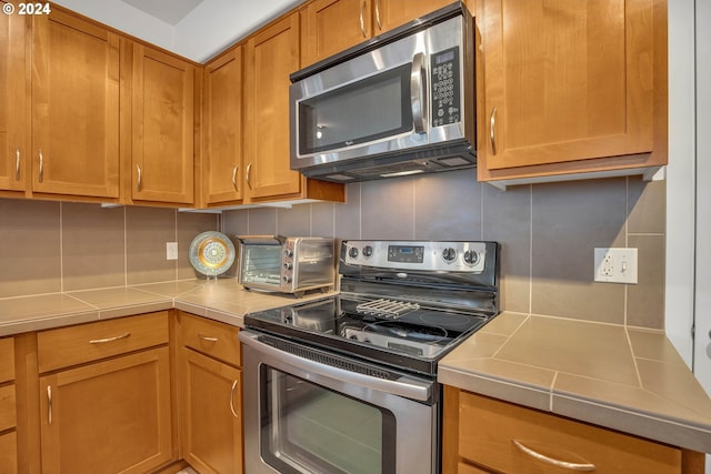 kitchen with tasteful backsplash, brown cabinets, a toaster, light countertops, and stainless steel appliances