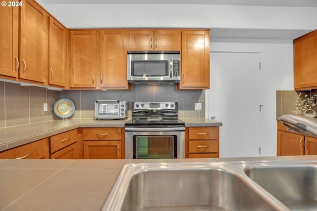 kitchen featuring brown cabinets, light countertops, stainless steel appliances, a toaster, and backsplash