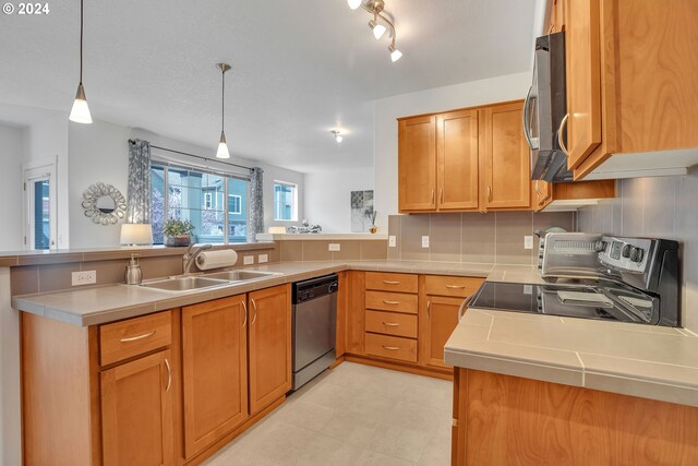 kitchen with appliances with stainless steel finishes, sink, kitchen peninsula, and decorative light fixtures