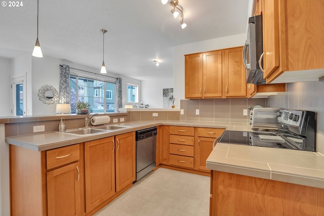 kitchen with pendant lighting, appliances with stainless steel finishes, a sink, light countertops, and a peninsula