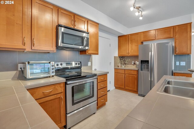 kitchen with tile counters, stainless steel appliances, sink, and backsplash