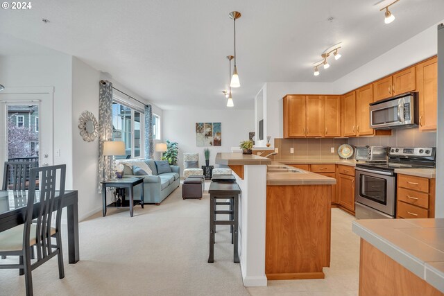 kitchen featuring kitchen peninsula, a kitchen breakfast bar, rail lighting, stainless steel appliances, and decorative light fixtures