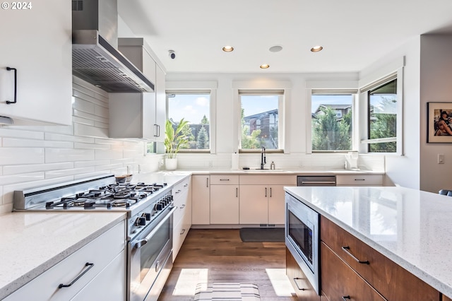 kitchen with sink, light stone counters, dark wood-type flooring, appliances with stainless steel finishes, and wall chimney exhaust hood