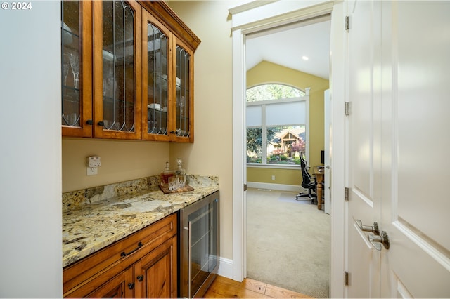 bar featuring wine cooler, light stone counters, vaulted ceiling, and light carpet