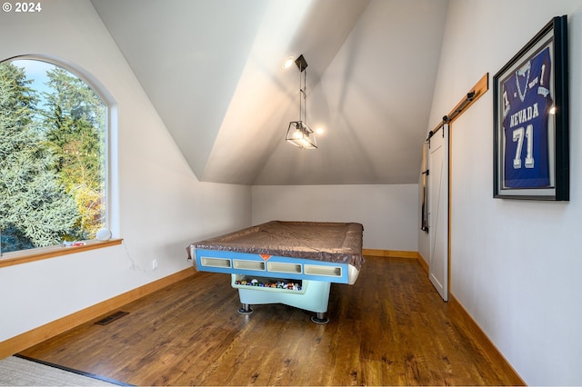 recreation room featuring dark wood-type flooring, vaulted ceiling, and a barn door