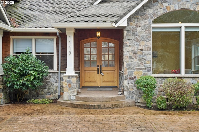 property entrance with stone siding, french doors, and roof with shingles