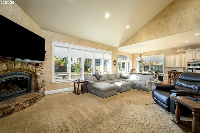 carpeted living room with a healthy amount of sunlight, high vaulted ceiling, an inviting chandelier, and a stone fireplace