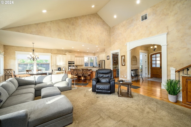 living room featuring a chandelier, high vaulted ceiling, plenty of natural light, and light wood-type flooring