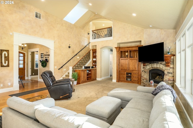 living room featuring a chandelier, a stone fireplace, light wood-type flooring, and high vaulted ceiling