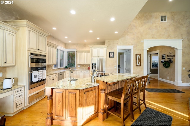 kitchen featuring a spacious island, stainless steel appliances, sink, light stone countertops, and light wood-type flooring