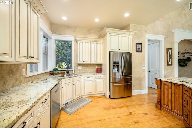 kitchen featuring appliances with stainless steel finishes, light wood-type flooring, sink, cream cabinetry, and light stone counters