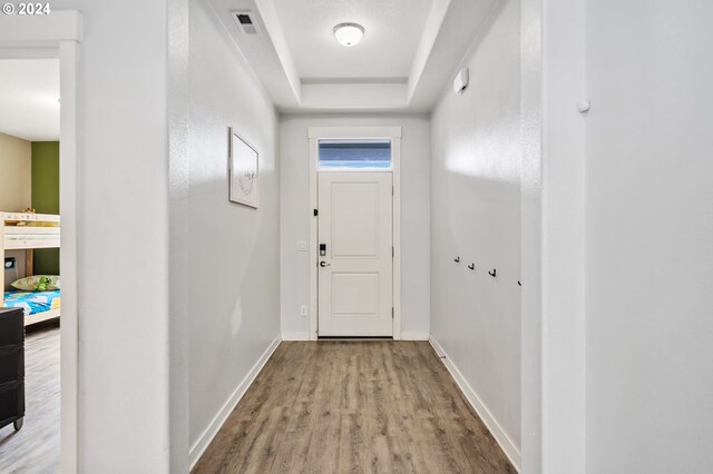 doorway to outside featuring a tray ceiling and light hardwood / wood-style floors