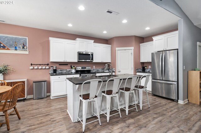 kitchen with light wood-type flooring, white cabinetry, stainless steel appliances, and a kitchen island with sink