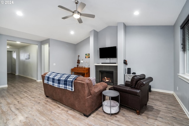 living room featuring lofted ceiling, a tiled fireplace, ceiling fan, and light wood-type flooring