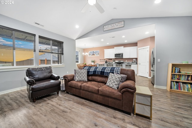 living room with vaulted ceiling, ceiling fan with notable chandelier, and light hardwood / wood-style floors