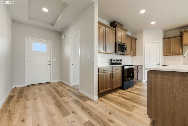 kitchen featuring stainless steel appliances, a tray ceiling, backsplash, and light hardwood / wood-style flooring