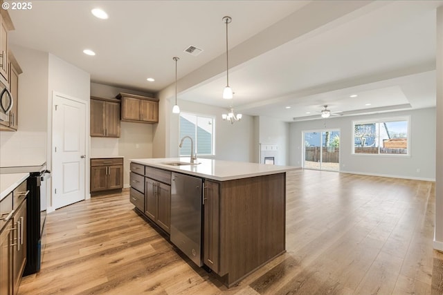 kitchen with sink, light hardwood / wood-style flooring, a kitchen island with sink, hanging light fixtures, and stainless steel appliances