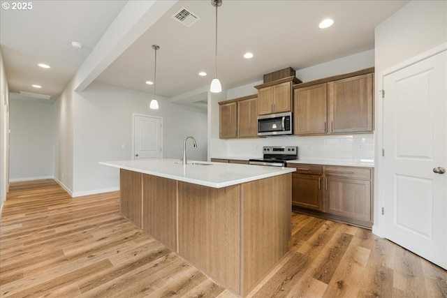 kitchen featuring sink, hanging light fixtures, a center island with sink, stainless steel appliances, and light hardwood / wood-style floors