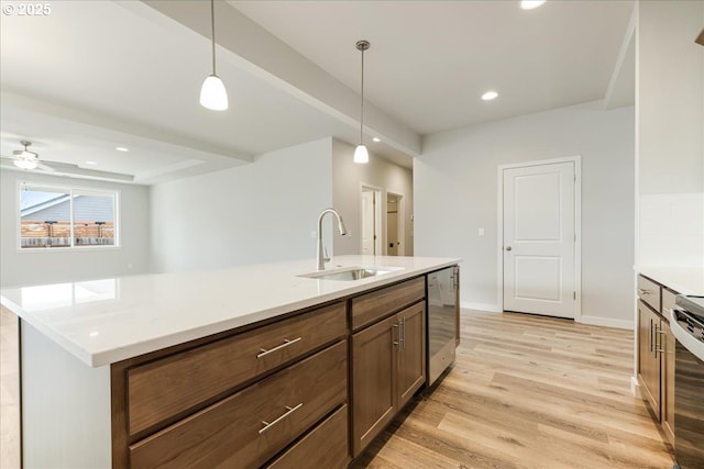 kitchen featuring pendant lighting, sink, a kitchen island with sink, stainless steel dishwasher, and light wood-type flooring