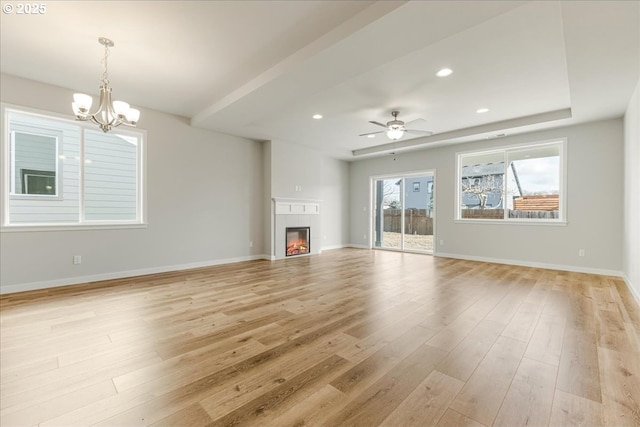 unfurnished living room with ceiling fan with notable chandelier, a fireplace, light wood-type flooring, and a tray ceiling