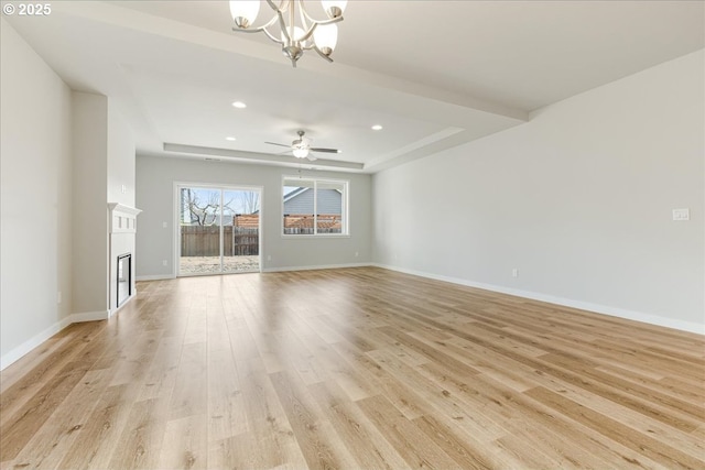 unfurnished living room featuring ceiling fan with notable chandelier, light hardwood / wood-style floors, and a raised ceiling