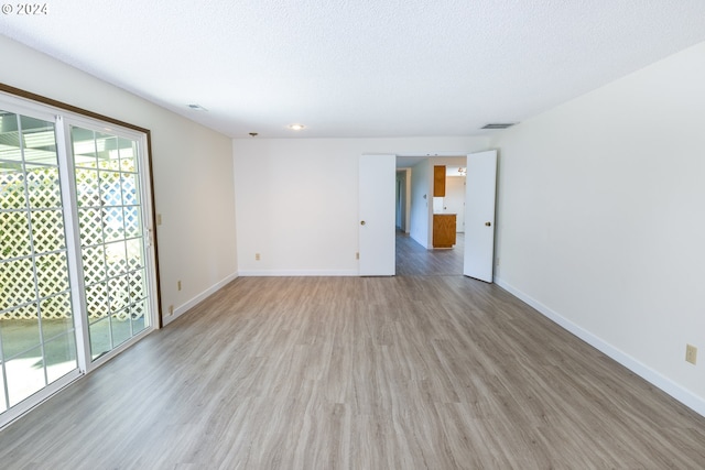 empty room with a textured ceiling and light hardwood / wood-style flooring