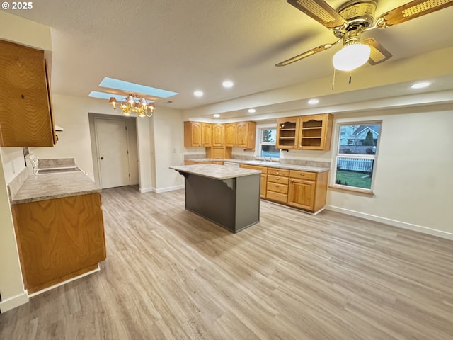 kitchen with a skylight, light wood-type flooring, a center island, ceiling fan, and a textured ceiling