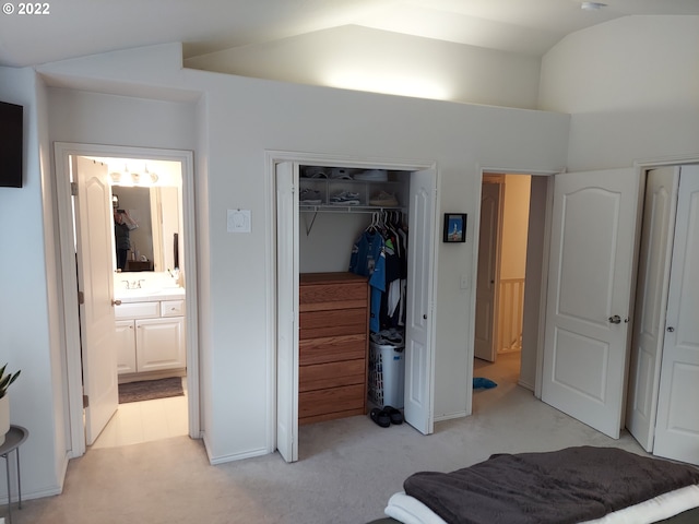 carpeted bedroom featuring connected bathroom, vaulted ceiling, a closet, and sink