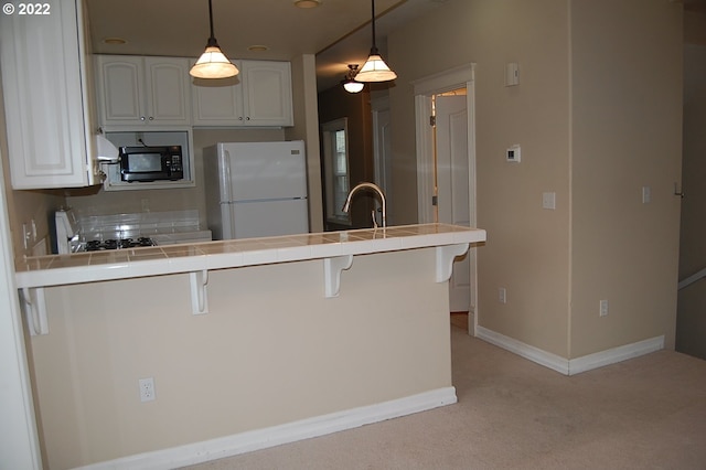 kitchen with kitchen peninsula, tile countertops, white fridge, white cabinetry, and a breakfast bar area