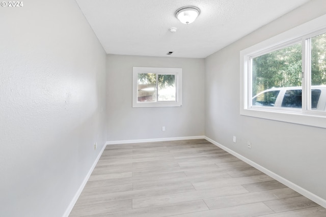 unfurnished room featuring plenty of natural light, a textured ceiling, and light wood-type flooring