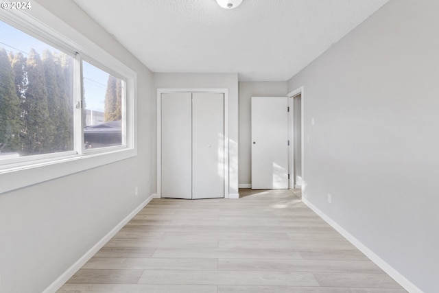 unfurnished bedroom with a textured ceiling, light hardwood / wood-style floors, and a closet