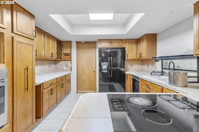 kitchen with a raised ceiling, backsplash, black fridge, and sink