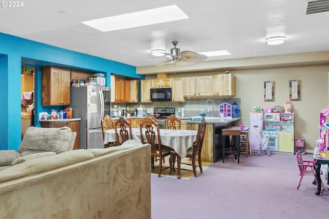 kitchen with a kitchen breakfast bar, ceiling fan, appliances with stainless steel finishes, tasteful backsplash, and light colored carpet