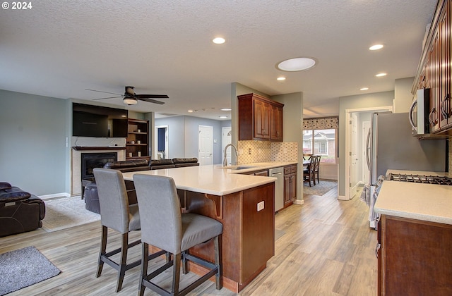 kitchen with kitchen peninsula, light hardwood / wood-style flooring, a kitchen breakfast bar, ceiling fan, and appliances with stainless steel finishes