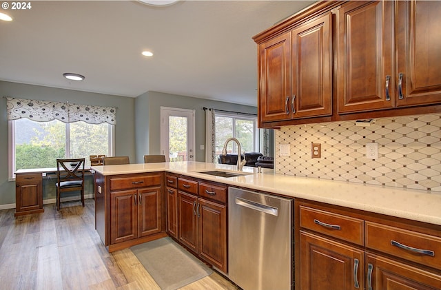 kitchen featuring sink, kitchen peninsula, backsplash, stainless steel dishwasher, and light wood-type flooring