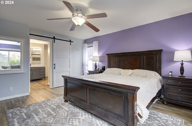 bedroom featuring a barn door, ensuite bathroom, ceiling fan, and light wood-type flooring