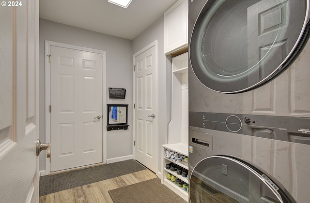 clothes washing area with cabinets, stacked washer and clothes dryer, and light wood-type flooring