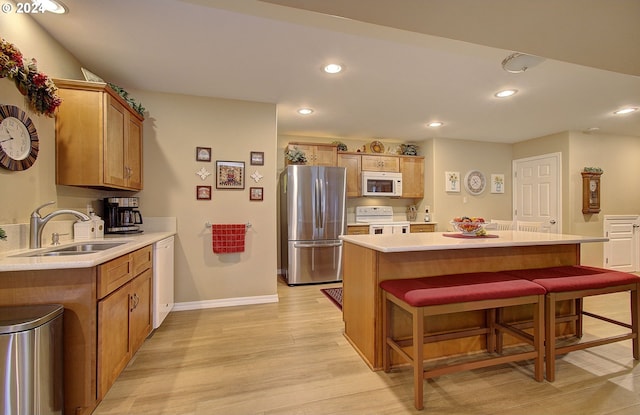 kitchen featuring light wood-type flooring, sink, a breakfast bar area, white appliances, and a center island